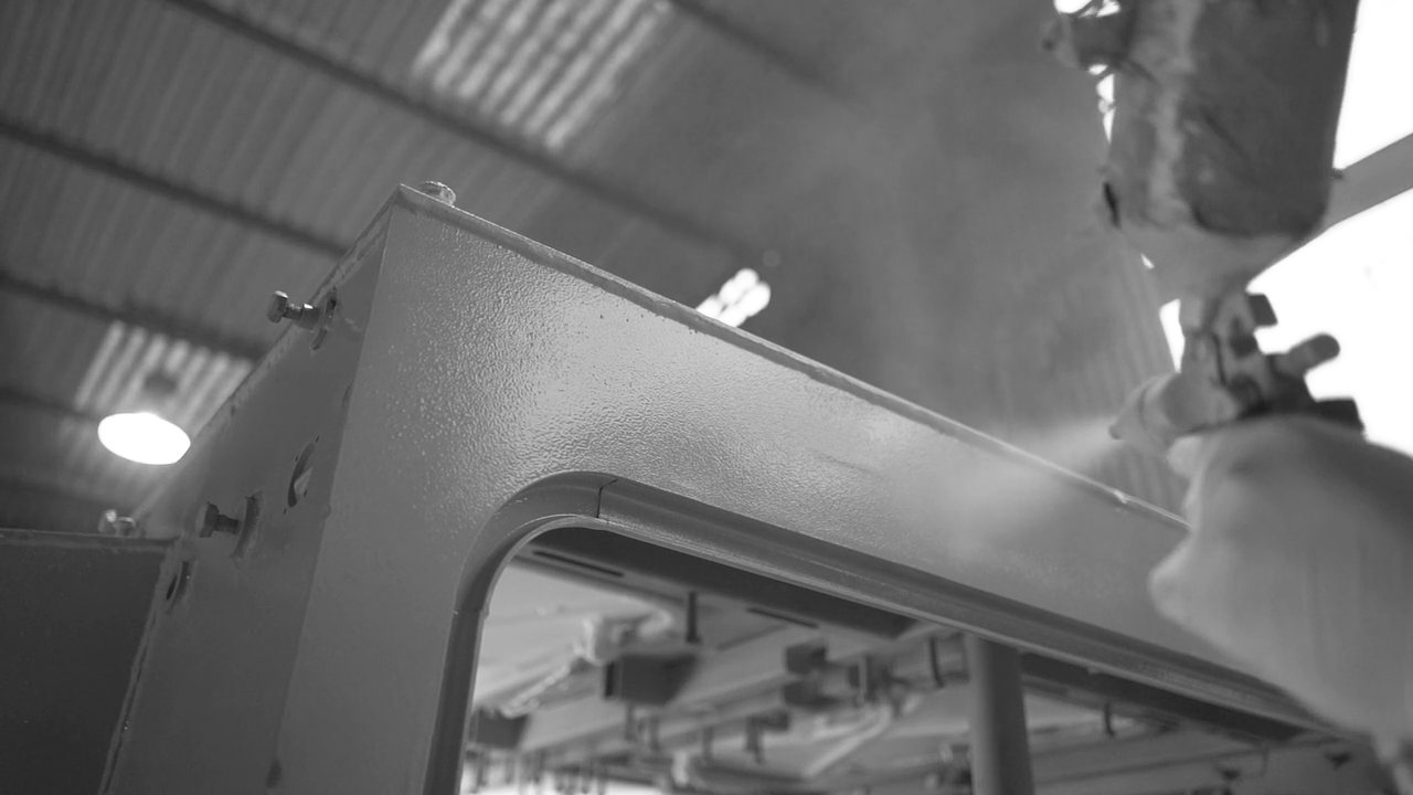 A spray gun laying a coat onto sheet metal on a factory floor